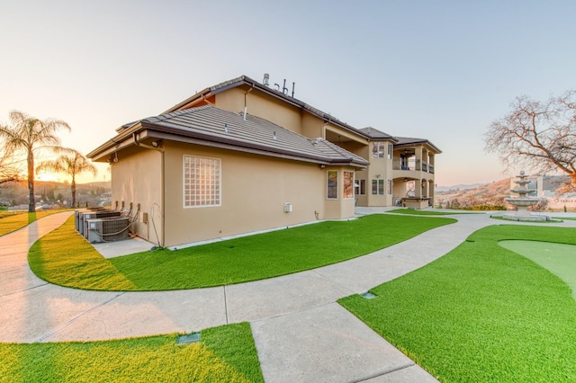 back house at dusk featuring a lawn, cooling unit, and a balcony