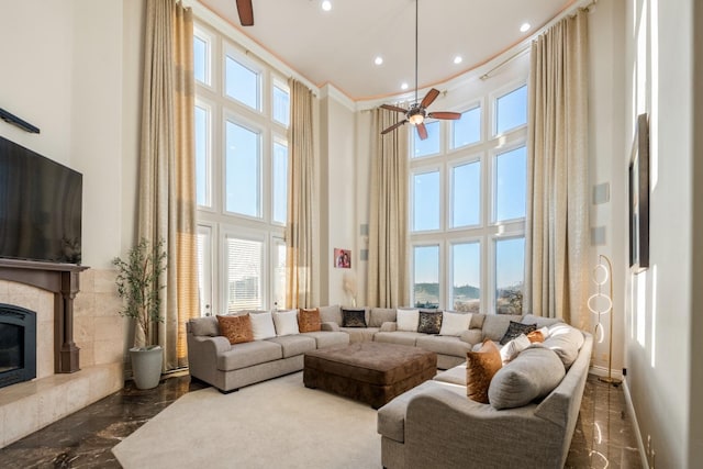 living room with ceiling fan, a high ceiling, and a tiled fireplace