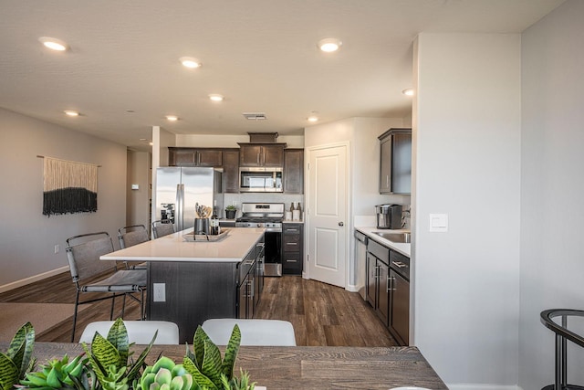 kitchen with appliances with stainless steel finishes, a kitchen breakfast bar, dark hardwood / wood-style flooring, a kitchen island, and dark brown cabinetry