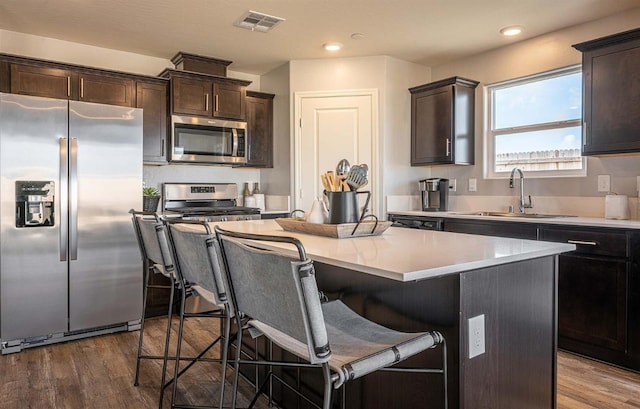 kitchen featuring appliances with stainless steel finishes, a kitchen island, sink, a kitchen breakfast bar, and dark hardwood / wood-style floors