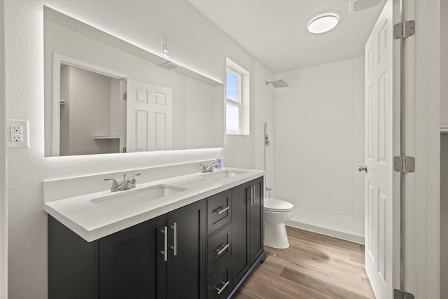 full bath with double vanity, wood finished floors, a sink, and toilet