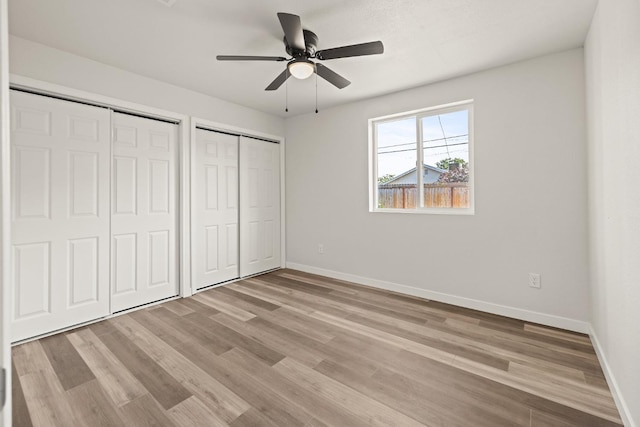 unfurnished bedroom with light wood finished floors, two closets, a ceiling fan, and baseboards