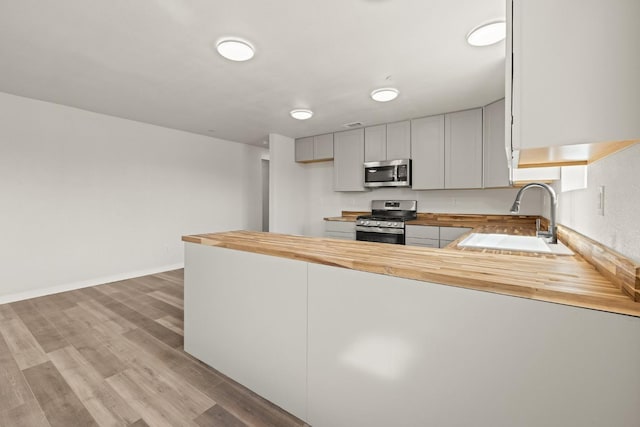 kitchen with wooden counters, light hardwood / wood-style floors, kitchen peninsula, sink, and appliances with stainless steel finishes