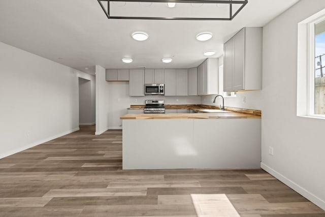 kitchen with wood counters, stainless steel appliances, kitchen peninsula, and sink