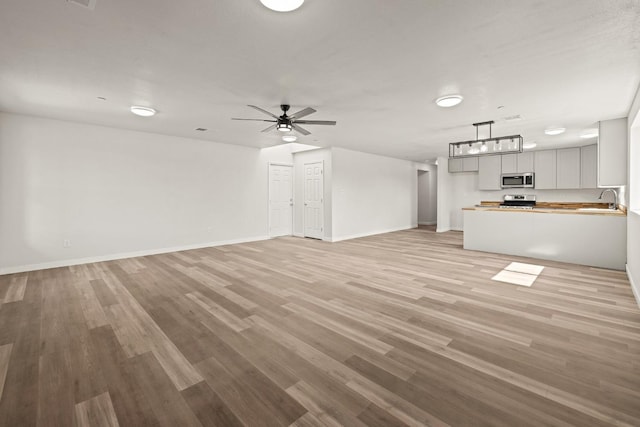 unfurnished living room with ceiling fan, light hardwood / wood-style flooring, and sink