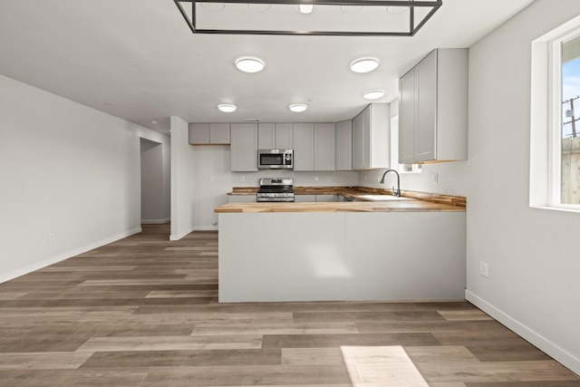 kitchen featuring stainless steel appliances, gray cabinets, a sink, wood counters, and a peninsula