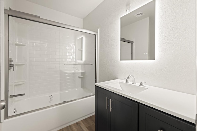 full bath with shower / bath combination with glass door, visible vents, a textured wall, vanity, and wood finished floors