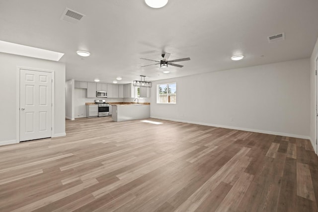 unfurnished living room featuring ceiling fan, baseboards, visible vents, and light wood-style floors