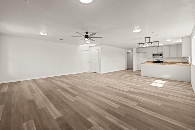 unfurnished living room with light wood-style floors, ceiling fan, baseboards, and a sink