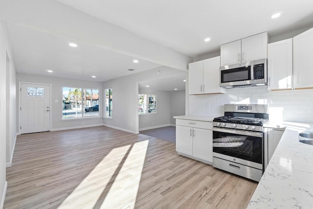 kitchen with light wood-type flooring, stainless steel appliances, white cabinetry, and tasteful backsplash