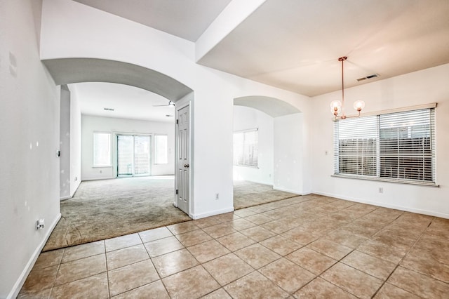 tiled spare room featuring ceiling fan with notable chandelier