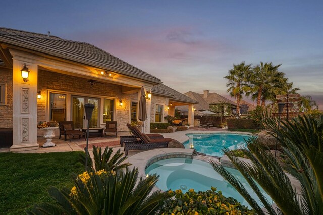 pool at dusk with a patio and an in ground hot tub