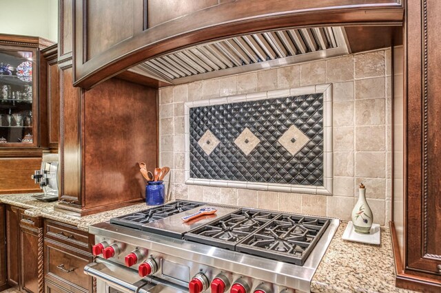 kitchen with ventilation hood, backsplash, light stone counters, and high end stainless steel range oven