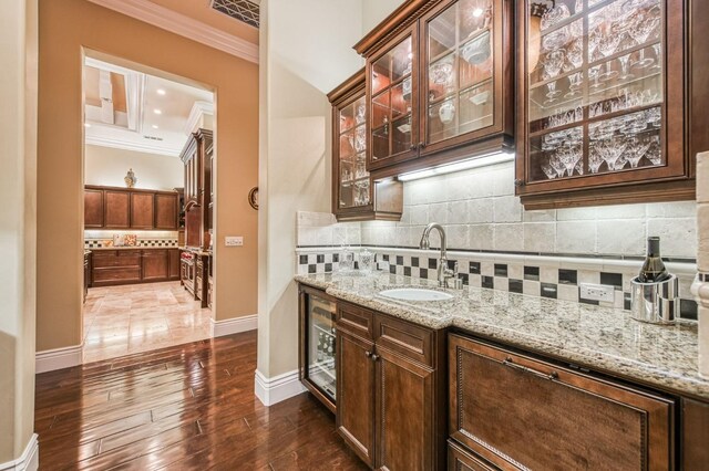 bar featuring tasteful backsplash, light stone countertops, sink, and crown molding