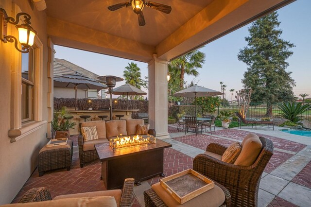 patio terrace at dusk featuring ceiling fan and an outdoor living space with a fire pit