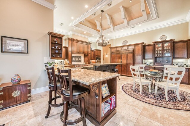 kitchen with decorative light fixtures, an island with sink, a tray ceiling, and ornamental molding