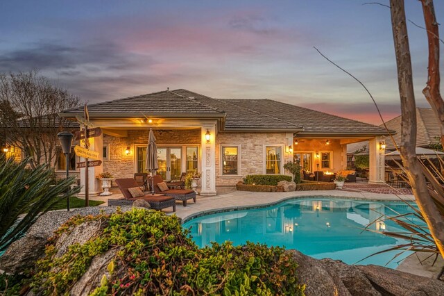 pool at dusk with an outdoor living space, french doors, and a patio