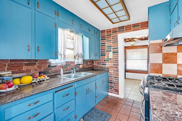 kitchen featuring brick wall, blue cabinetry, stainless steel range with gas stovetop, and sink