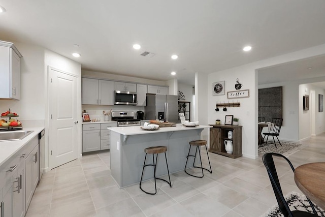 kitchen with a kitchen bar, sink, a kitchen island with sink, gray cabinetry, and stainless steel appliances