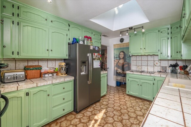 kitchen with sink, backsplash, black electric stovetop, tile counters, and stainless steel fridge with ice dispenser