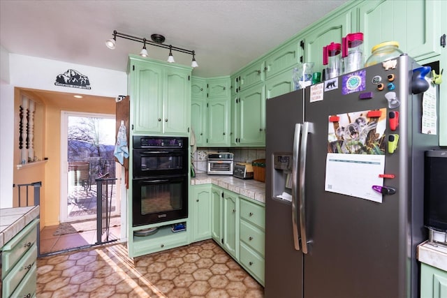 kitchen featuring tile countertops, black double oven, green cabinetry, and stainless steel refrigerator with ice dispenser