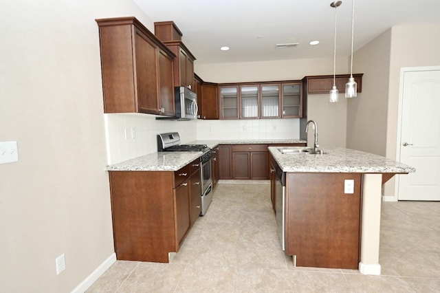 kitchen featuring pendant lighting, stainless steel appliances, backsplash, light stone counters, and a center island with sink