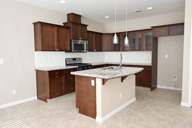 kitchen with a center island with sink, appliances with stainless steel finishes, tasteful backsplash, light stone countertops, and sink