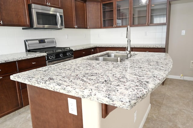 kitchen with appliances with stainless steel finishes, a kitchen bar, sink, light stone counters, and light tile patterned floors