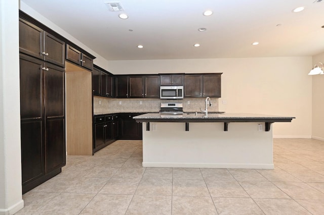 kitchen with an island with sink, stainless steel appliances, a kitchen breakfast bar, dark brown cabinetry, and sink