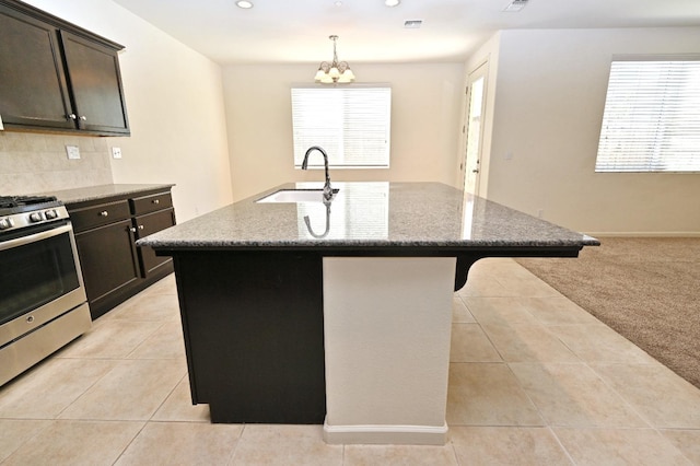 kitchen with light carpet, sink, dark stone counters, and an island with sink