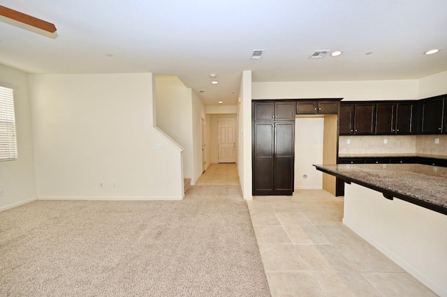 kitchen with dark brown cabinets, light tile patterned flooring, tasteful backsplash, and dark stone countertops