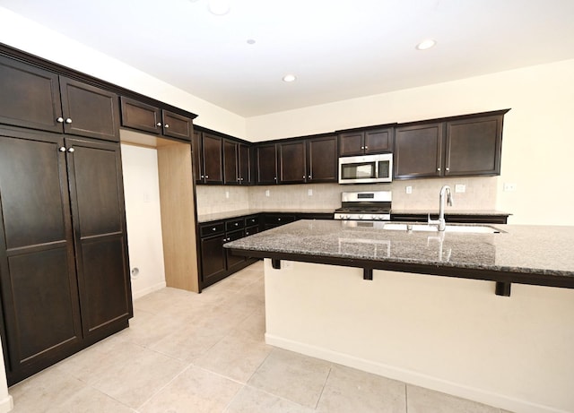 kitchen with a kitchen breakfast bar, appliances with stainless steel finishes, sink, and dark stone counters