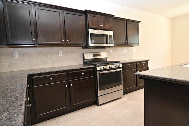 kitchen featuring light tile patterned floors, appliances with stainless steel finishes, dark brown cabinetry, and dark stone counters