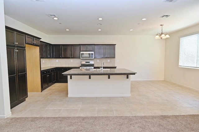 kitchen with light tile patterned floors, a kitchen bar, an island with sink, stainless steel appliances, and decorative backsplash