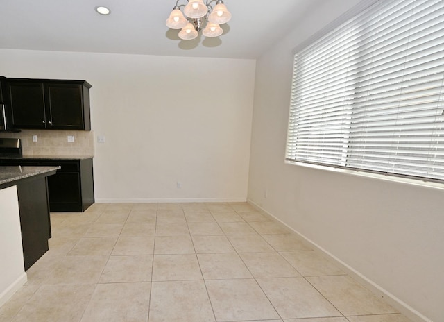 kitchen with tasteful backsplash, a notable chandelier, light tile patterned flooring, and light stone counters