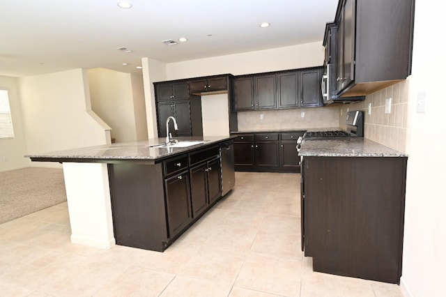 kitchen featuring a center island with sink, appliances with stainless steel finishes, tasteful backsplash, stone countertops, and sink