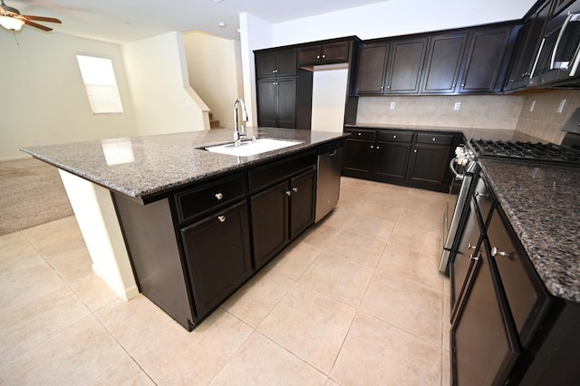 kitchen featuring a center island with sink, appliances with stainless steel finishes, decorative backsplash, dark stone counters, and sink