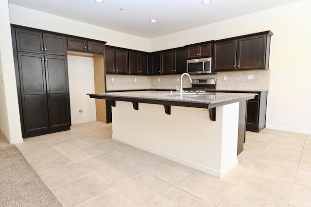 kitchen featuring sink, appliances with stainless steel finishes, a center island with sink, and dark brown cabinets