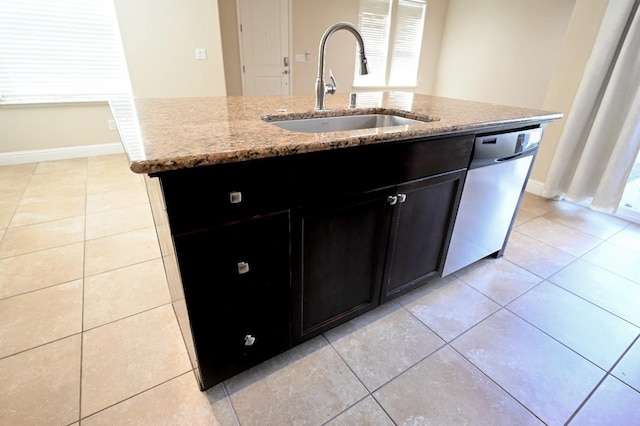 kitchen with light stone countertops, sink, light tile patterned floors, stainless steel dishwasher, and a center island with sink