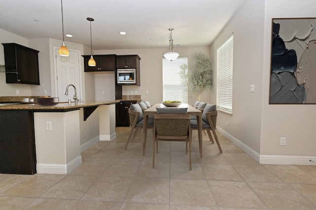 kitchen featuring stainless steel microwave, dark stone countertops, pendant lighting, a breakfast bar, and sink