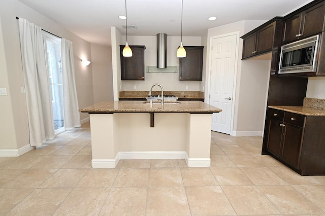 kitchen featuring stainless steel microwave, decorative light fixtures, stone countertops, and wall chimney range hood