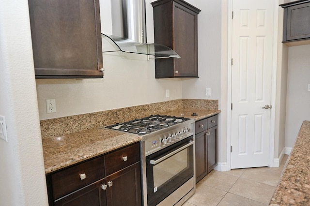 kitchen with light tile patterned floors, gas range, dark brown cabinets, wall chimney exhaust hood, and light stone counters