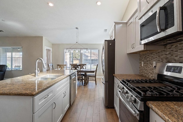 kitchen with pendant lighting, a center island with sink, sink, white cabinetry, and appliances with stainless steel finishes