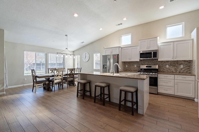 kitchen featuring white cabinetry, a breakfast bar area, appliances with stainless steel finishes, a kitchen island with sink, and vaulted ceiling