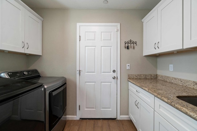 laundry area with washer and clothes dryer, wood-type flooring, and cabinets