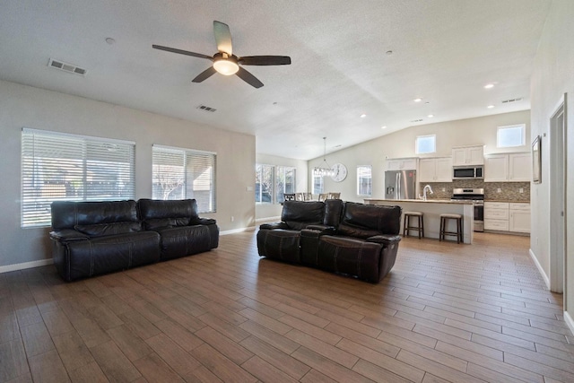 living room with ceiling fan with notable chandelier, sink, lofted ceiling, and a healthy amount of sunlight