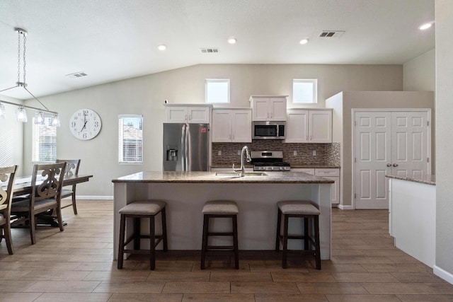 kitchen with white cabinetry, stainless steel appliances, sink, vaulted ceiling, and a center island with sink