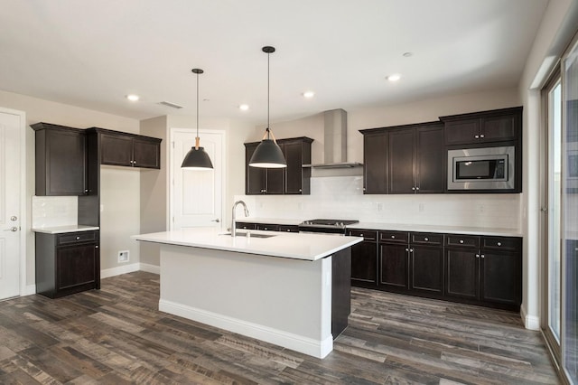 kitchen with pendant lighting, appliances with stainless steel finishes, wall chimney exhaust hood, an island with sink, and sink