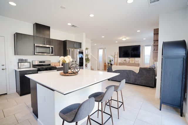 kitchen with light tile patterned floors, appliances with stainless steel finishes, a breakfast bar, and a center island