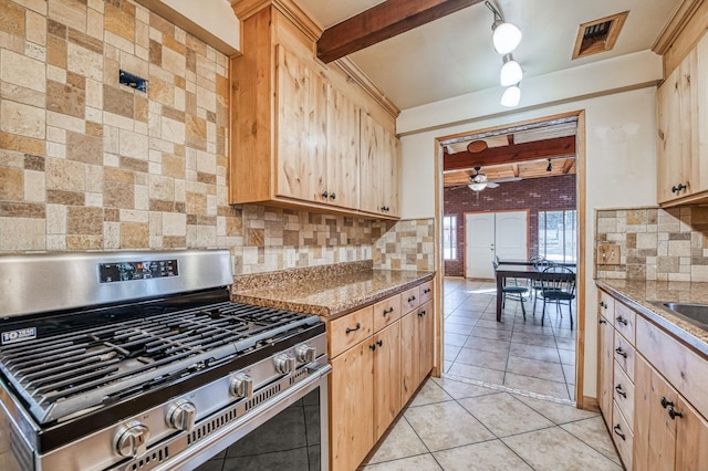 kitchen featuring decorative backsplash, light brown cabinets, light stone counters, and stainless steel gas range oven